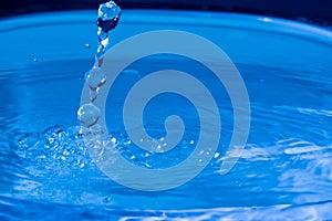 Water splash in dark blue color with a drop of water flying from