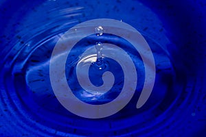 Water splash in dark blue color with a drop of water flying from