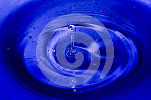 Water splash in dark blue color with a drop of water flying from