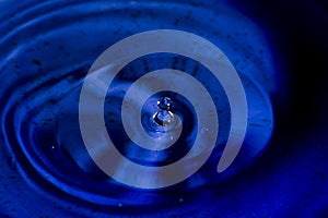 Water splash in dark blue color with a drop of water flying from