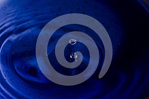 Water splash in dark blue color with a drop of water flying from