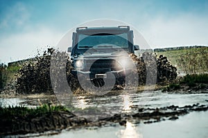 Water splash in off-road racing. Classic 4x4 car crossing water with splashes on muddy road. Low angle view of front of