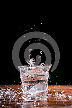 Water splash with transparent glass on wooden table with black background. Copy space for your text