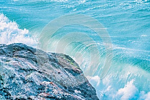 Water splashes close up. Crystal clear sea water beats against the rocks. Sea waves break on the stone shore of the ocean, blue