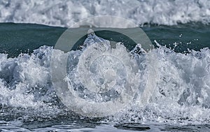 Water splashes on sea/ocean wave crest against blurred bac