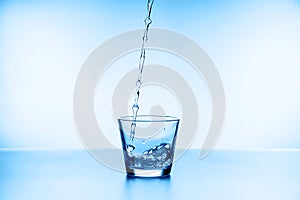 Water splashing from glass isolated on blue background