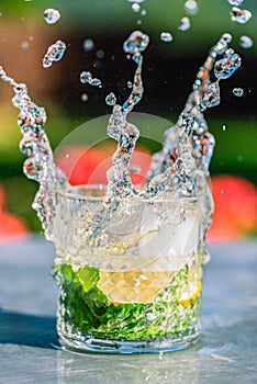 Water splashing from glass with mint, standing on metal table in garden with blurred background