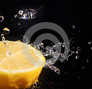 Water splashing over half a lemon. Black background.