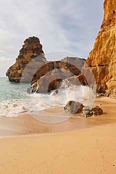 Water splashing over large rocks on sandy shore in Portugal