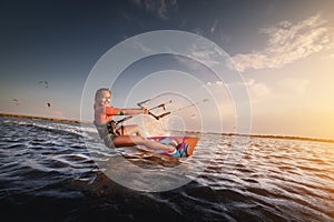 Water sports. The girl is engaged in kitesurfing with a kite in the sky on board in the blue sea, riding the waves with