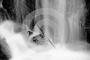 Water spray below small waterfall on mountain stream, water is falling over mossy boulder. The spray create on level and gravel mi