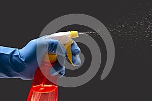 Water sprayer bottle in a hand in a protective glove spraying liquid on a dark background. household items for home