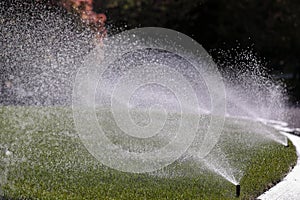 Water sprays from an automatic lawn sprinkler system over green lawn