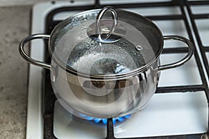 The water in a stainless steel pot is heated on a gas