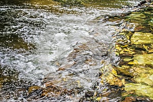 Water stream flowing past rock and stones in the river.