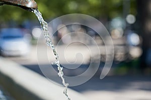 Water Stream in fontain with blurred street on a background bokeh.