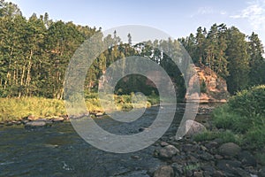 water stream in river of Amata in Latvia with sandstone cliffs, green foliage - vintage retro film look