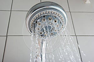 Water streaming out of silver round shower head inside bathroom. Low angle close up shot, no people