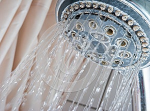 Water streaming out of silver round shower head inside bathroom. Low angle close up shot, no people