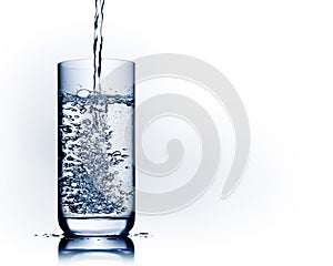 Water pouring into glass with bubbles and reflection on white