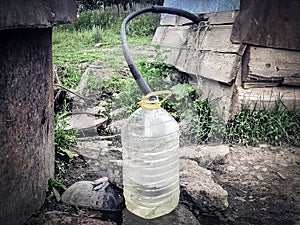 Water supply shortage and climate change threats: collecting drinking water with 5 liter plastic water bottle from a well in a rur