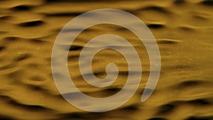 Water surface colored by golden light moving creating waves under ultra sound vibrations, abstract background template.