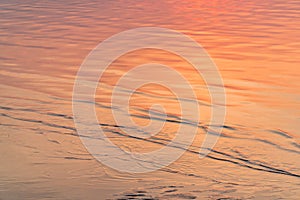 Water surface with waves reflecting orange light from sunset