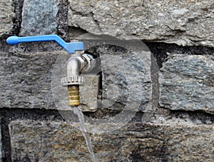 Water tap spigot on a rock blocks wall with running spilling water