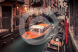 A water taxi passes under a small bridge on a narrow canal in Venice, Italy
