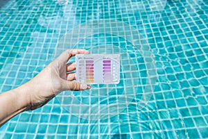 Water test kit in girl hand over blurred clean and clear swimming pool water