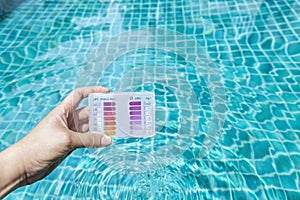 Water testing test kit in girl hand over crystal clear swimming pool water background