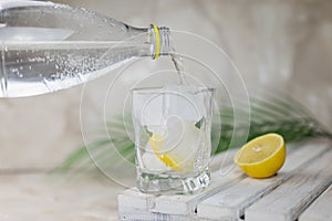 Water or tonic is poured from a bottle into a glass with ice photo