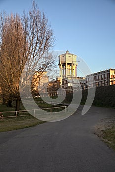 Water tower in the distance among buildings framed by trees seen from a path in a park
