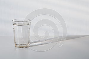 Water in transparent faceted glass and  it`s shadow on gray background. purified fresh drink water and its refraction