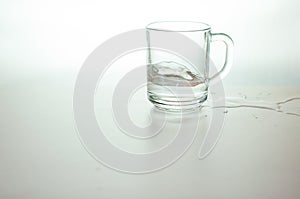 Water in transparent glass and puddle on gray background. purified fresh drink water on table