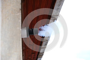 Water vapor from a gas central heating boiler flue condenses in cold air. The flue vents through the exterior wall of a building.