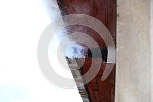 Water vapor from a gas central heating boiler flue condenses in cold air. The flue vents through the exterior wall of a building.