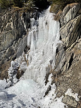 water of a waterfall frozen into a solid ice mass against grey rocks