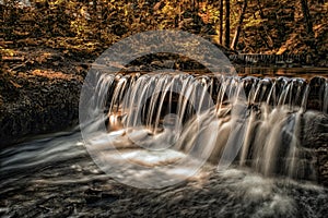 Waterfall in the autumn forest is illuminated by the sunbeams