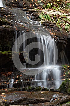 Waterfall cascading across wet rocks dotted with autumn leaves and moss