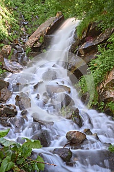 Waterfall and clear river in a mountain stream in a green rocky forest. vertical image