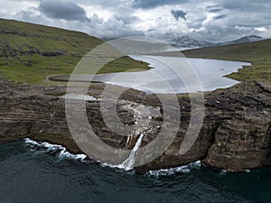 Waterfall and Cliffs of Traelanipa with the lake above the ocean, Faroe Islands, Denmark, Europe, aerial view