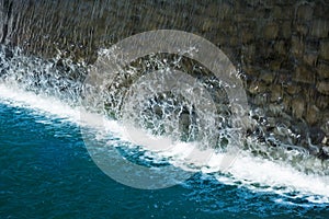 Waterfall close up image. Splashes and foam on blue water surface from fallen vertical cascade flow