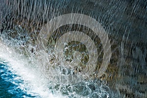 Waterfall close up image. Splashes and foam on blue water surface from fallen vertical cascade flow