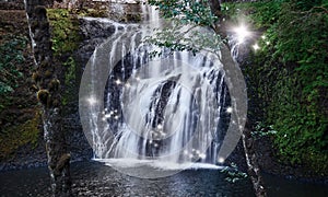 Waterfall with dancing fairy lights in enchanted forest