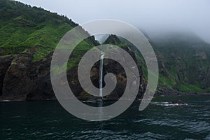 Waterfall dropping from high rocky cliffs into the ocean Sea of Okhotsk around the Shiretoko Peninsula