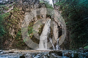 A waterfall falls from a cliff in the jungle among the green vegetation. spring melting of glaciers