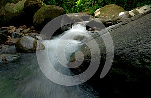 Waterfall is flowing in jungle. Rock or stone at waterfall. Waterfall in tropical forest. Nature background. Green season travel.