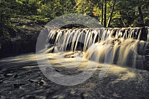 Waterfall in a forest is illuminated by the sunbeams. Closeup shot