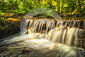 Waterfall in a forest is illuminated by the sunbeams. Closeup shot